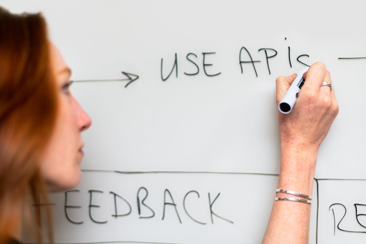 services-02 A woman writes 'Use APIs' on a whiteboard, focusing on software planning and strategy.